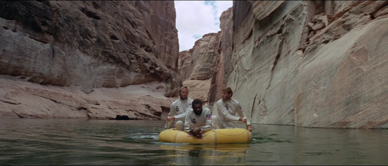 Planet of the Apes (1968) (1968) movie still: wide — Three men in flight suits float down a calm river flanked by high canyon walls. They sit inside…