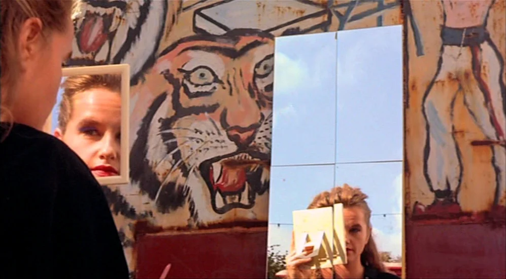 Roselyne and the Lions (1989) movie still: medium — A woman stands in front of a weathered circus backdrop featuring painted tigers. She holds a…