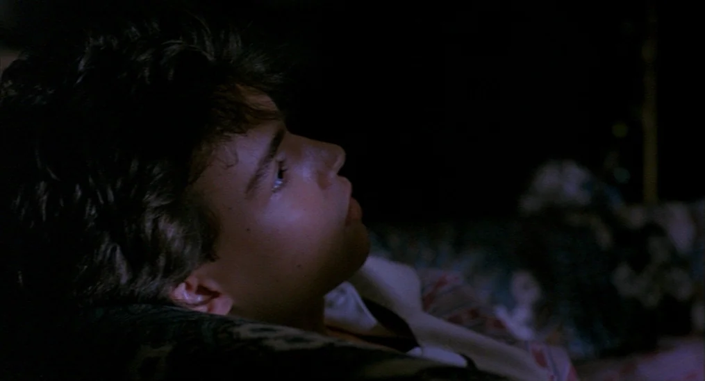 A Nightmare On Elm Street (1984) movie still: closeup — A dimly lit room with heavy shadows hides the surrounding environment from view. A young…