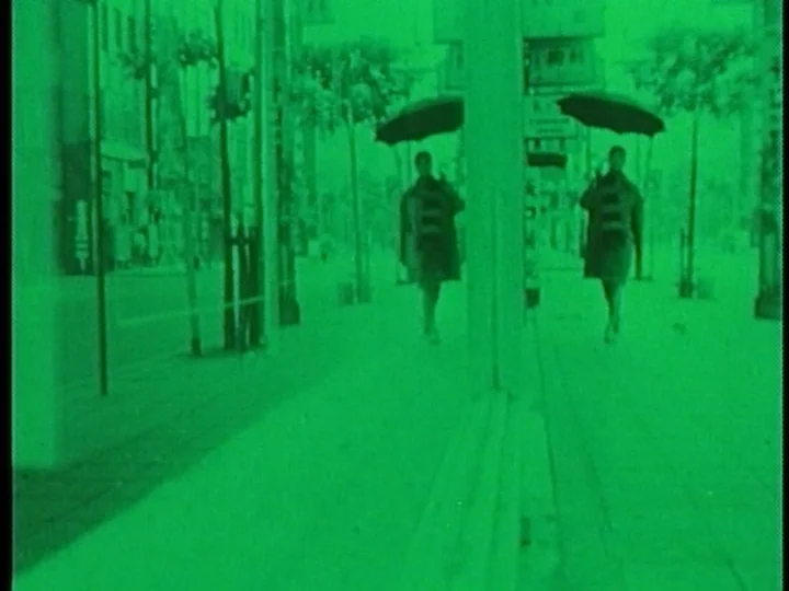 The Cage (1964) movie still: wide — A quiet urban sidewalk lined with buildings is bathed in a monochrome green light. A lone figure walks towards…