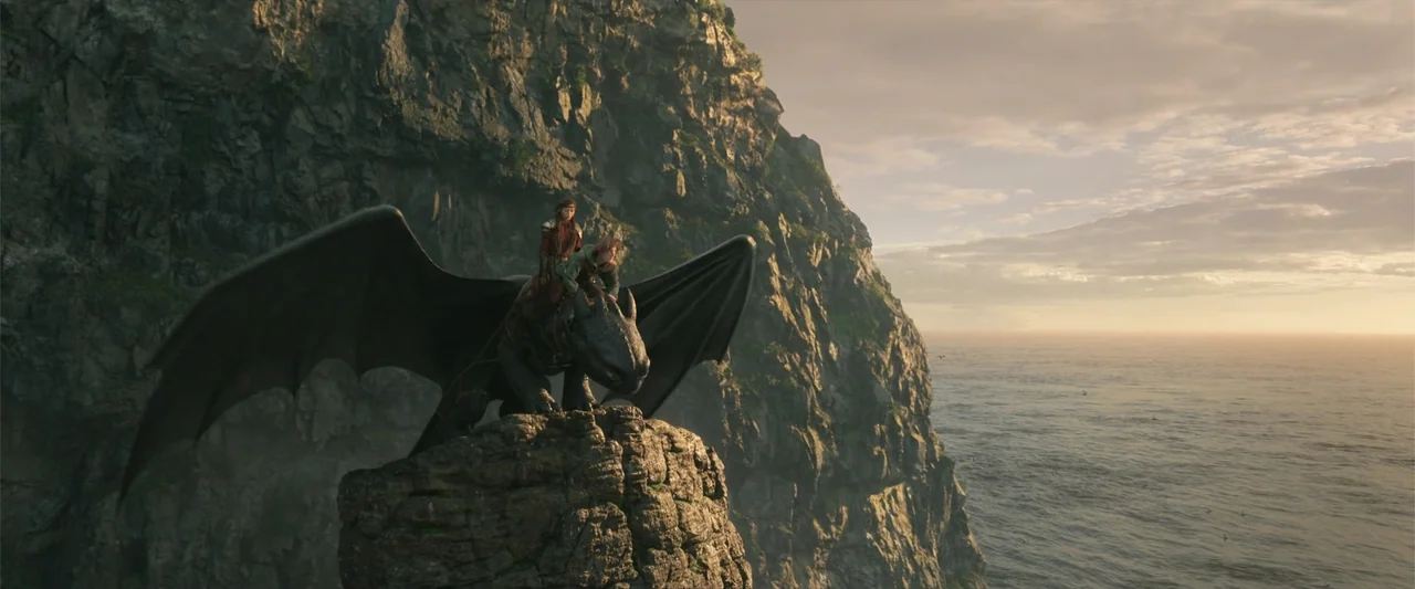 How to Train Your Dragon (2025) movie still: wide — A rugged cliff face rises sharply from the ocean during golden hour. A large black dragon stands…