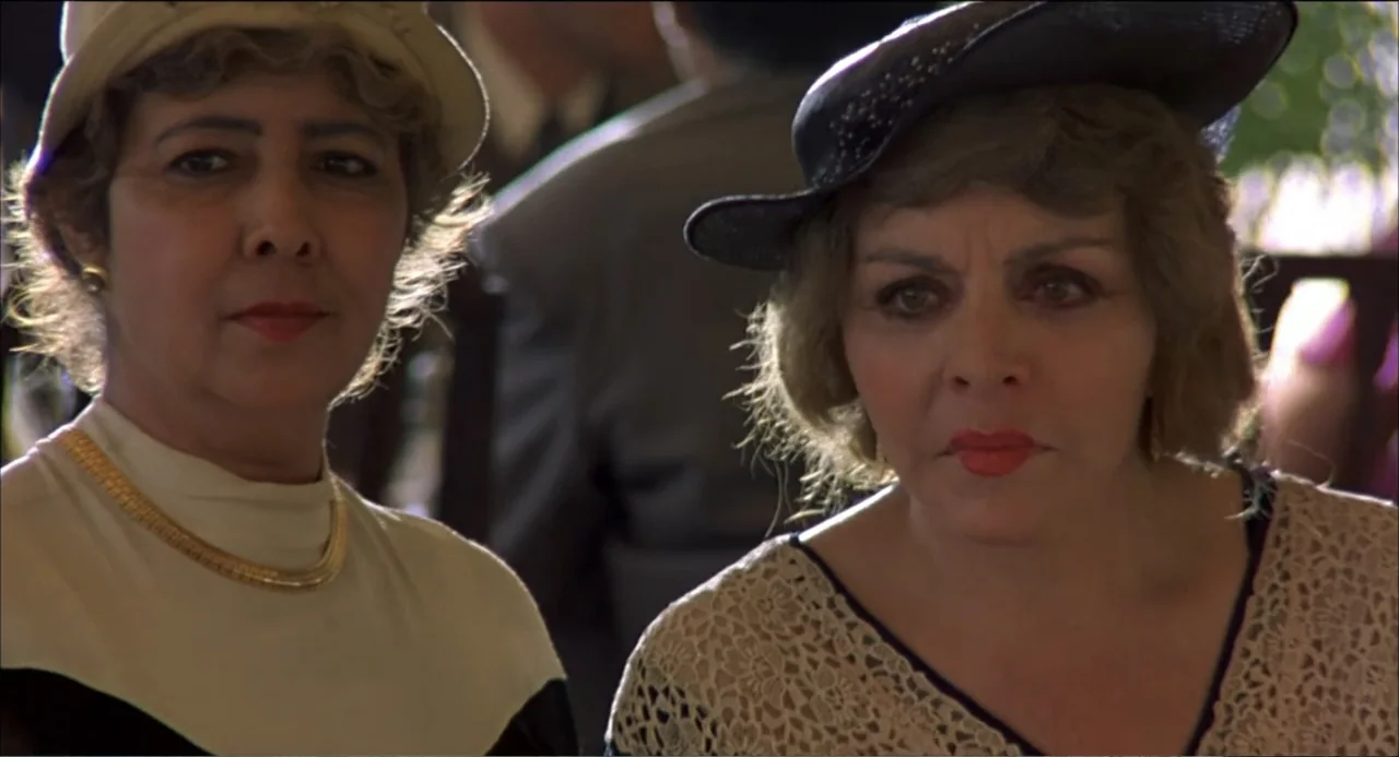 Like Water for Chocolate (1992) movie still: medium — Two older women sit outdoors at an outdoor cafe wearing 1930s style hats. The women look…