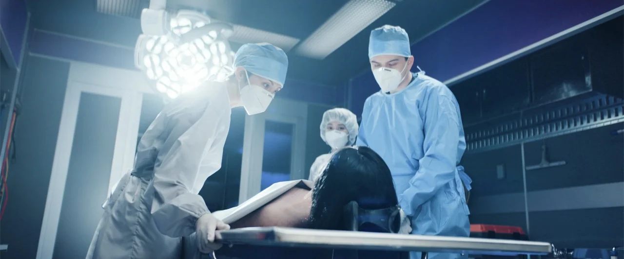 Angel Flight THE MOVIE (2026) movie still: medium — An operating room features large overhead surgical lights, dark wall tiling, and stainless…