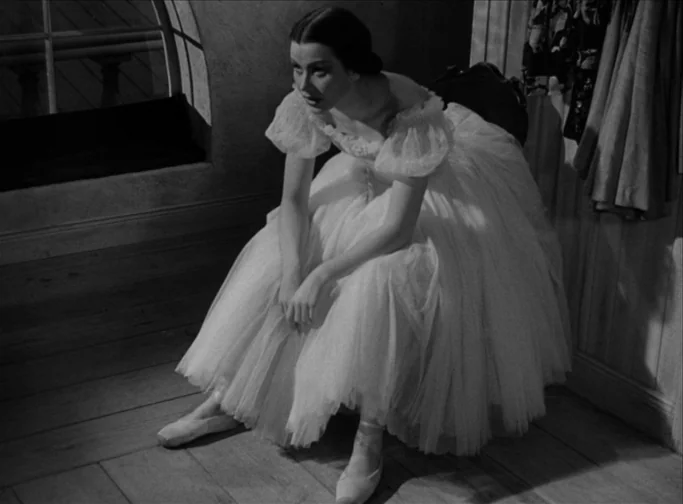 Summer Interlude (1951) movie still: fullbody — A dimly lit room features a wooden floor and a rounded window frame. A woman in a white tulle dress…