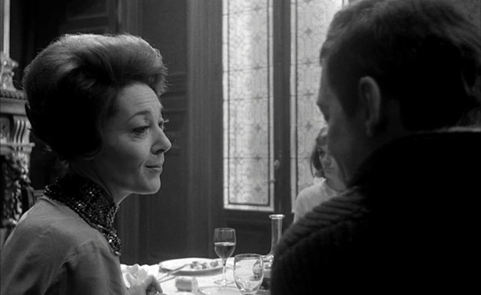 Le Feu Follet (1963) movie still: medium — A formal dining room interior with a glass panelled door and a table setup. A woman faces an unseen man…