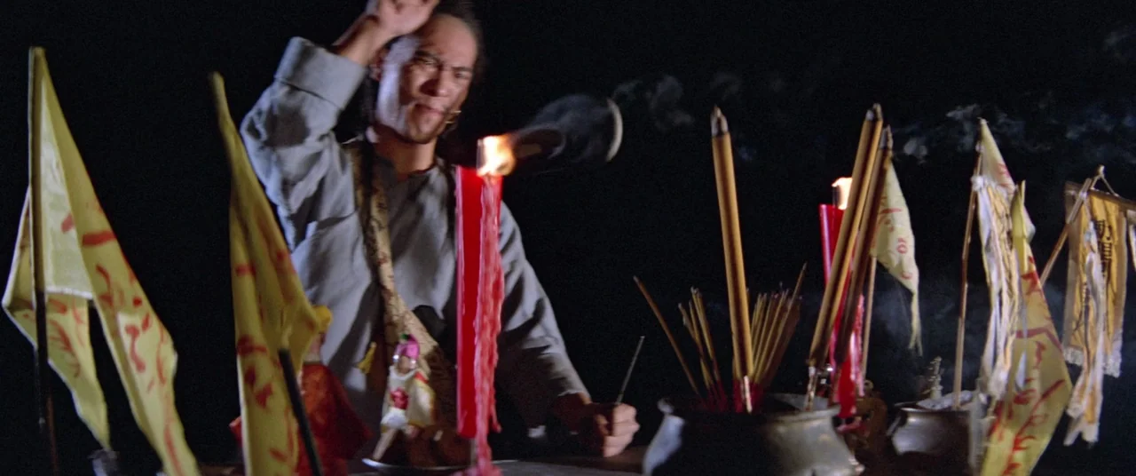 Encounter of the Spooky Kind (1980) movie still: medium — A dark space features a ritual altar adorned with yellow banners and red candles. A man…