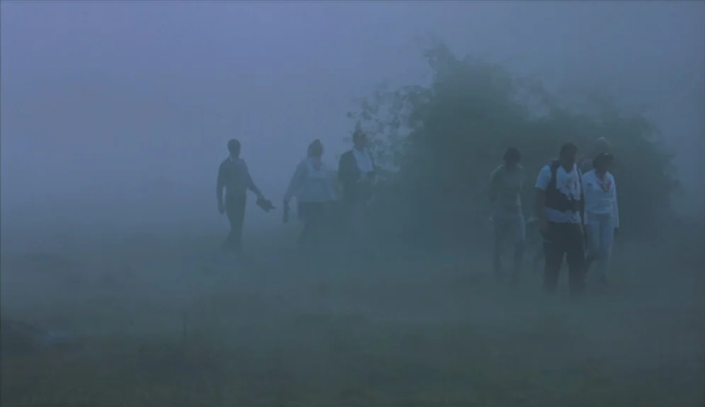 A Swedish Love Story (1970) movie still: wide — A group of people walk through a field shrouded in a thick layer of fog. Sparse vegetation and…