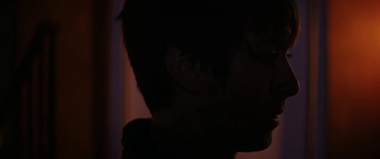 Super Dark Times (2017) movie still: closeup — A dark, dimly lit interior space with minimal architectural detail visible in the shadows. A person…
