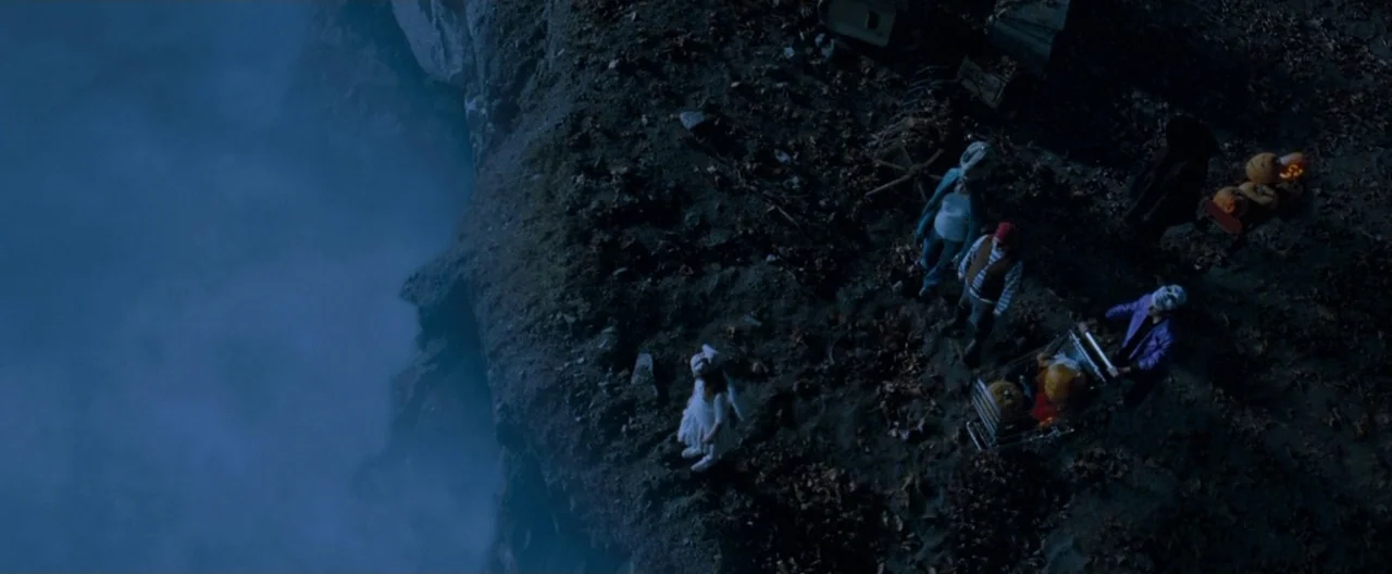 Trick ‘R Treat (2007) movie still: wide — A high-angle view shows several figures in costumes standing on a dark, cliff edge. Thick blue mist rises…