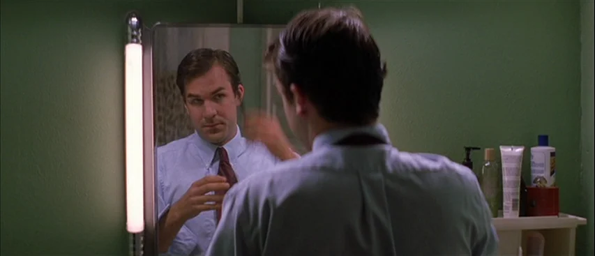All The Real Girls (2003) movie still: medium — A small bathroom features solid olive-green walls and a vertical mirror light fixture. A man in a…