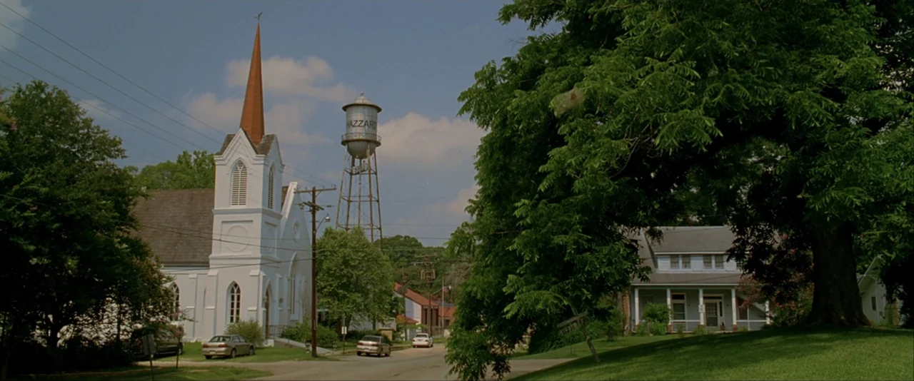 The Dukes of Hazzard (2005) movie still: establishing — A rural town square features a white church and a prominent water tower. Mature trees…
