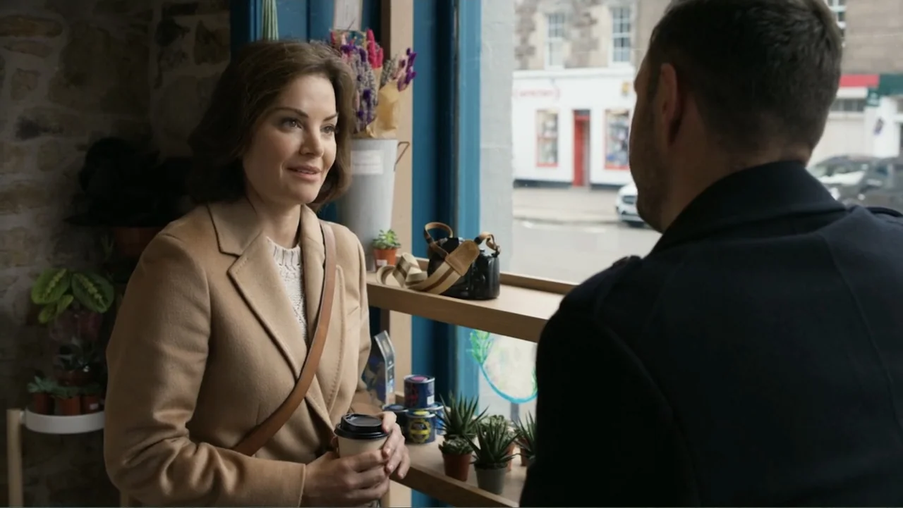 A Scottish Love Scheme (2024) movie still: medium — A bright coffee shop interior features stone walls and shelves lined with small potted plants. A…