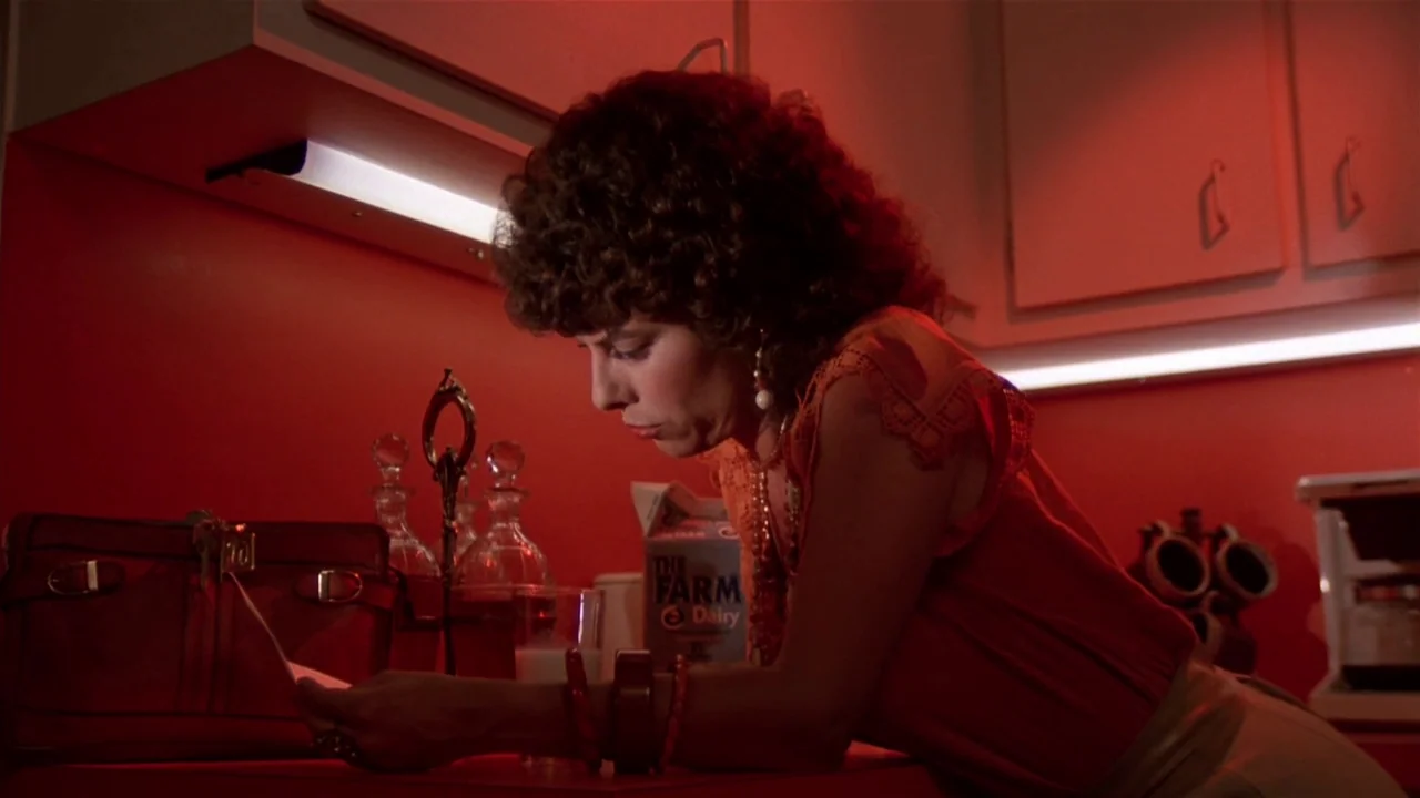 Creepshow (1982) movie still: medium — A dimly lit room with saturated red walls and white cabinet fronts. A woman stands at a counter looking down…