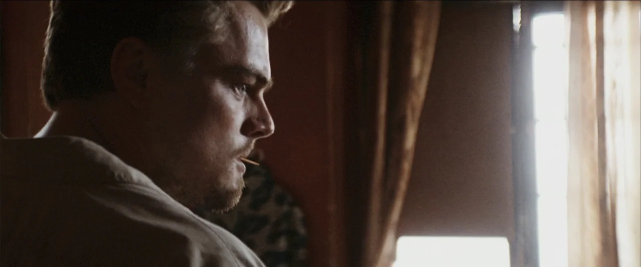 Blood Diamond (2006) movie still: closeup — A dimly lit interior space with a window covered by a thin curtain. A man in profile stands near the…