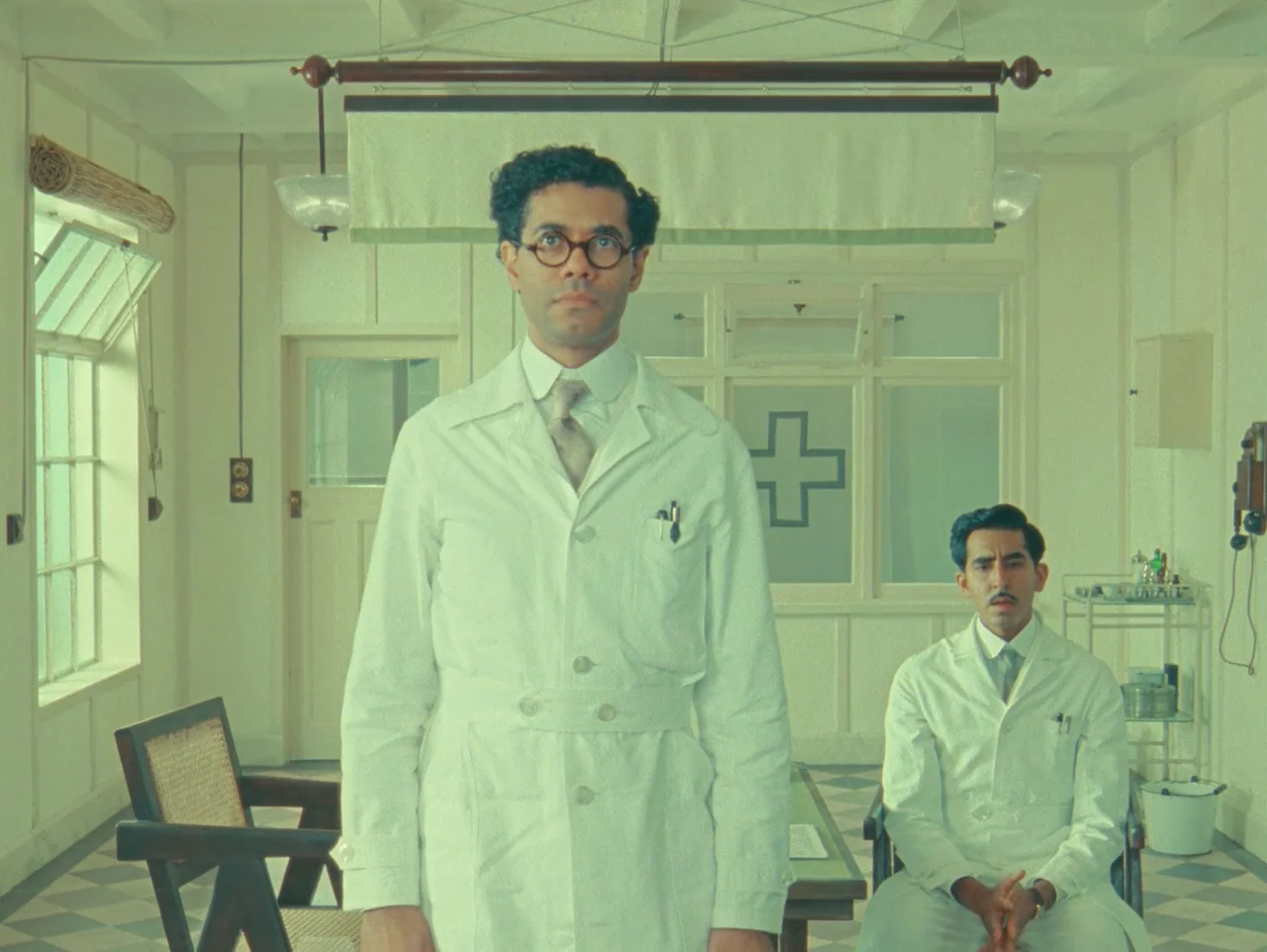 The Wonderful Story of Henry Sugar (2023) movie still: medium — A medical office with light-colored walls and a classic black-and-white checkered…