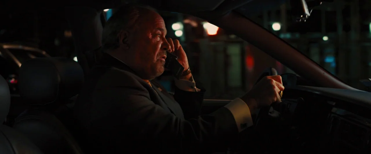 The Wolf of Wall Street (2013) movie still: medium — The interior of a moving vehicle at night with blurred city lights visible outside. An older…
