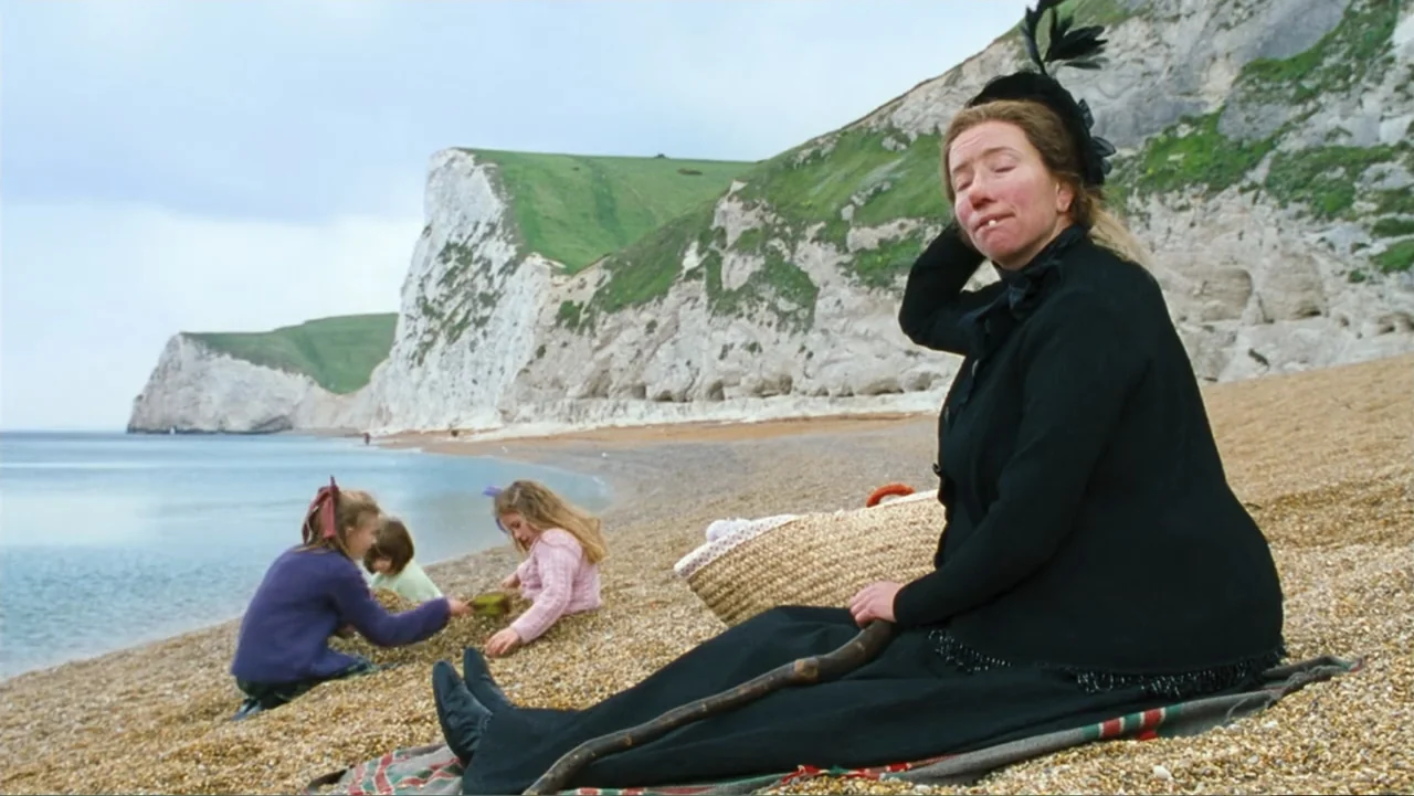 Nanny McPhee and the Big Bang (2010) movie still: medium — A pebble beach sits beneath tall chalk cliffs under a cloudy daytime sky. A woman in…