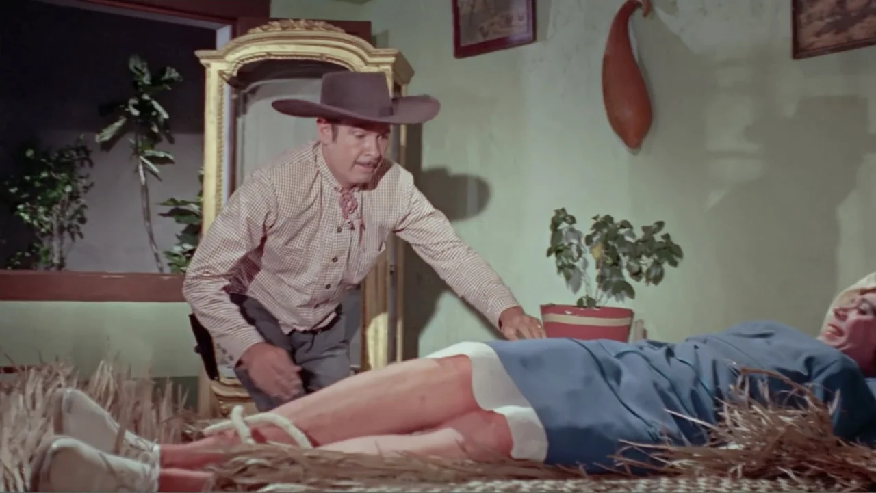 Los Dos Rivales (1966) movie still: medium — An interior space with light-colored walls contains straw strewn across the floor area. A man wearing a…
