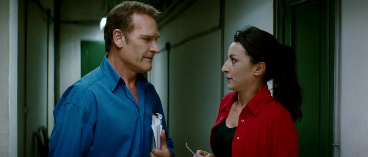 Broken Embraces (2009) movie still: medium — A narrow white-walled corridor features dark green doors along the sides. A man and a woman stand in…