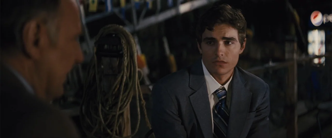Unfinished Business (2015) movie still: medium — A dimly lit wooden dock at night features blurred nautical ropes in the foreground. A young man in…