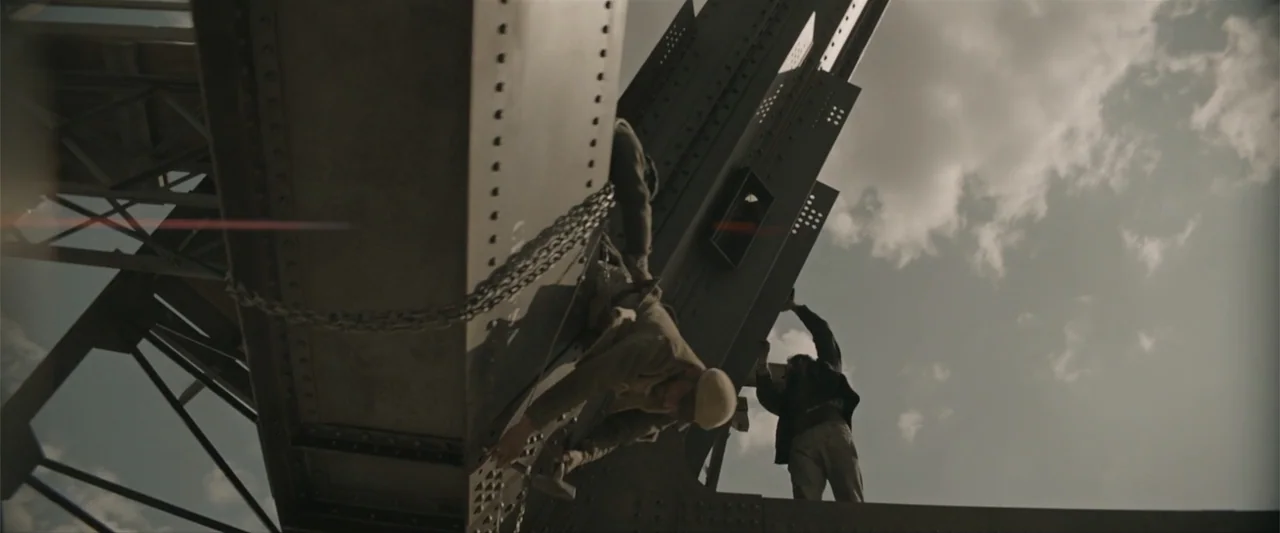 Eiffel (2021) movie still: wide — A high-angle view captures men working on the massive steel structure of a bridge. The workers are clinging to the…