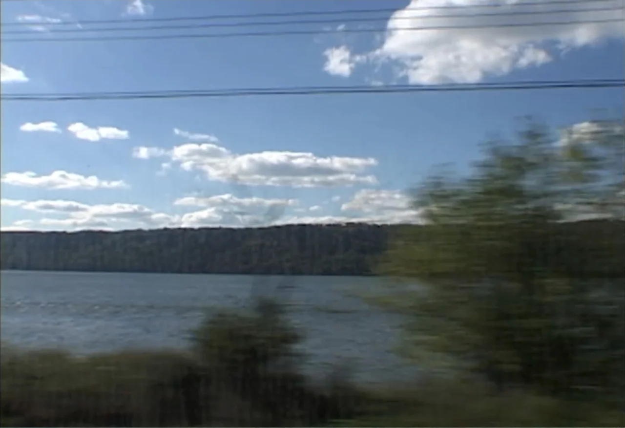 Dope Sick Love (2005) movie still: establishing — A wide view shows a large river bordered by a long wooded ridge. Motion blur affects the…