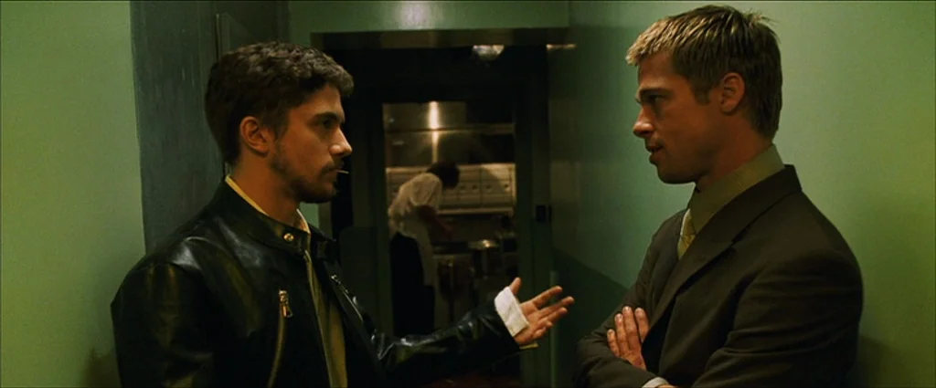 Ocean’s Eleven (2001) movie still: medium — A narrow corridor with green walls connects to a back kitchen area. Two men stand facing each other…