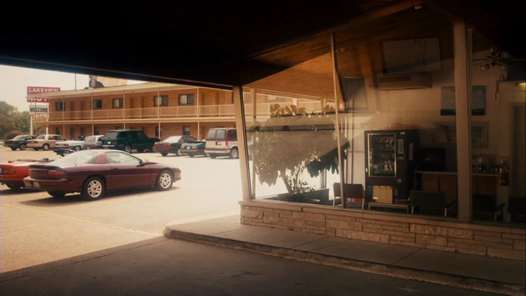 The Informant! (2009) movie still: establishing — A view from beneath a motel overhang looking out at a paved parking lot. Several passenger cars…