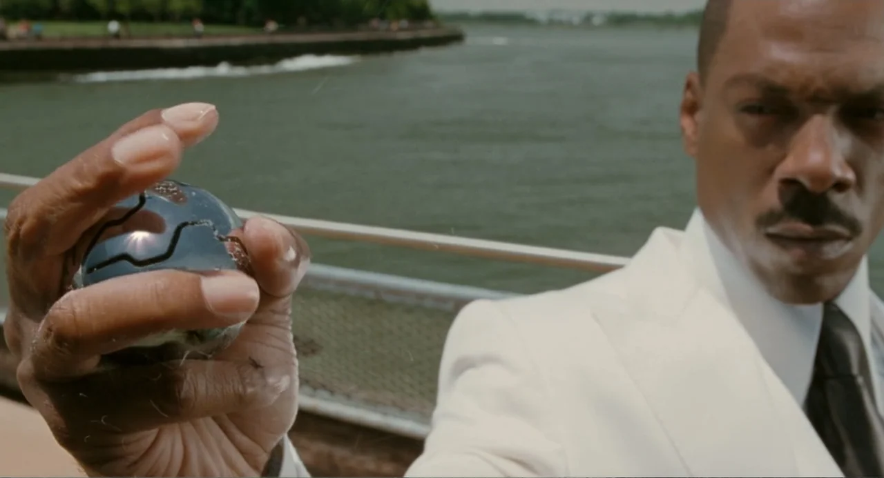 Meet Dave (2008) movie still: medium — A waterfront walkway bordered by a metal railing with a river in the background. A man in a white suit holds…