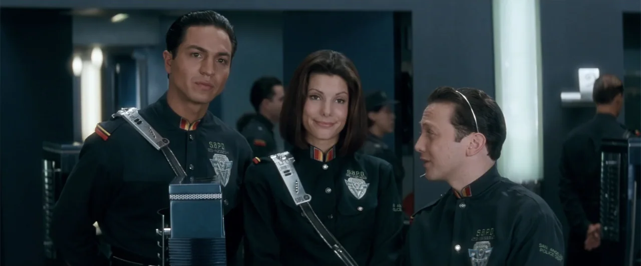 Demolition Man (1993) movie still: medium — A brightly lit futuristic police department interior with dark wall panels and metallic accents. Three…