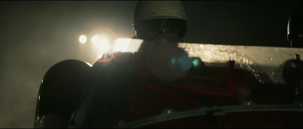 Ferrari (2023) movie still: medium — A dark night track interior looking out from the cockpit of a vintage race car. The driver is silhouetted…
