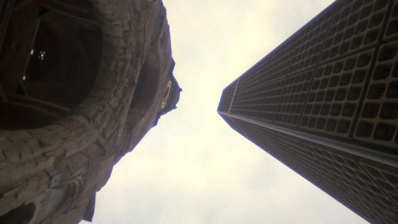 Powaqqatsi (1988) movie still: establishing — A stone historical tower stands across from a tall, modern office building. The structures reach…