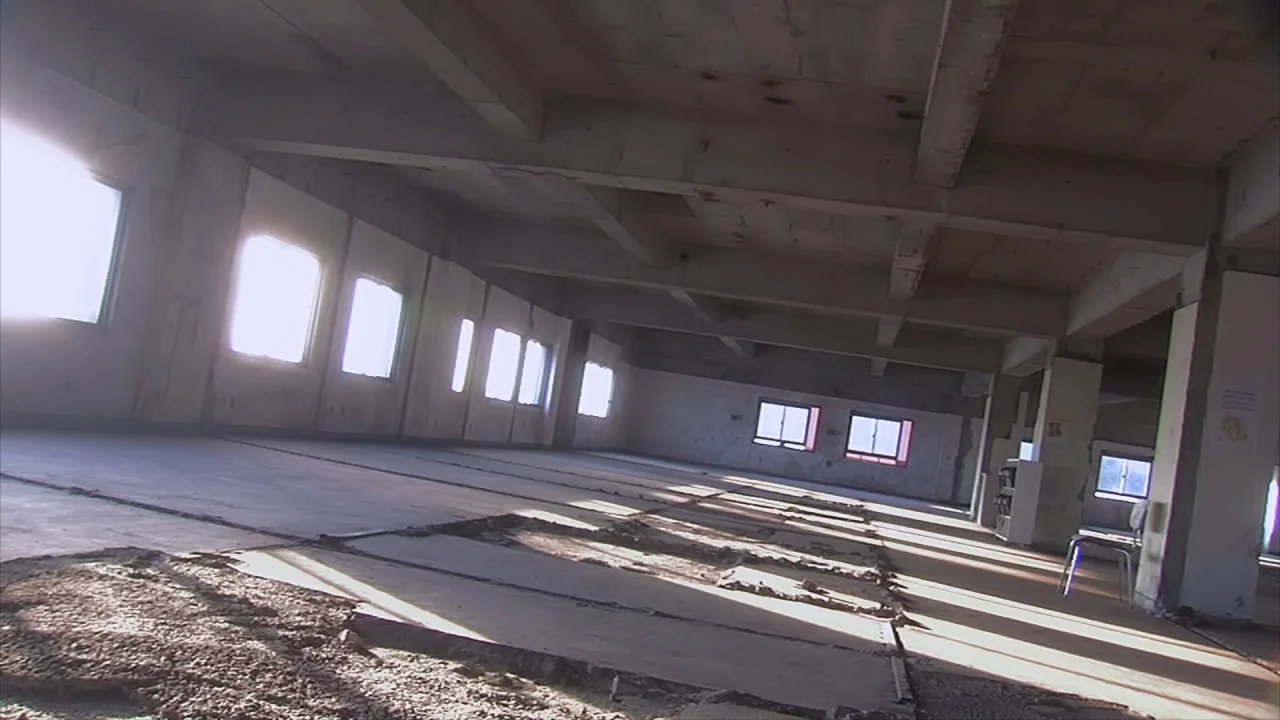 Tokyo Gore Police (2008) movie still: establishing — A spacious, unfinished concrete floor in an industrial structure has exposed beams and…
