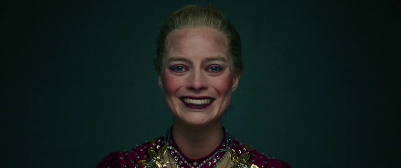 I, Tonya (2017) movie still: closeup — A dark background frames the upper torso of a woman in a theatrical costume. The woman maintains eye contact…