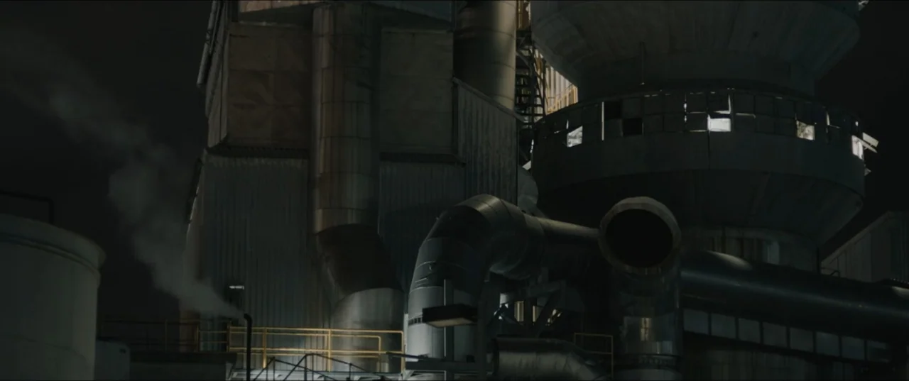 Death to Summer (2021) movie still: wide — An industrial facility features large cylindrical metal tanks, complex pipe systems, and steel walkways.…