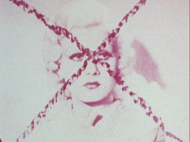 Emperor Tomato Ketchup movie still: closeup — A portrait of a woman is presented with a large, dark-red cross overlay. The image appears on a…