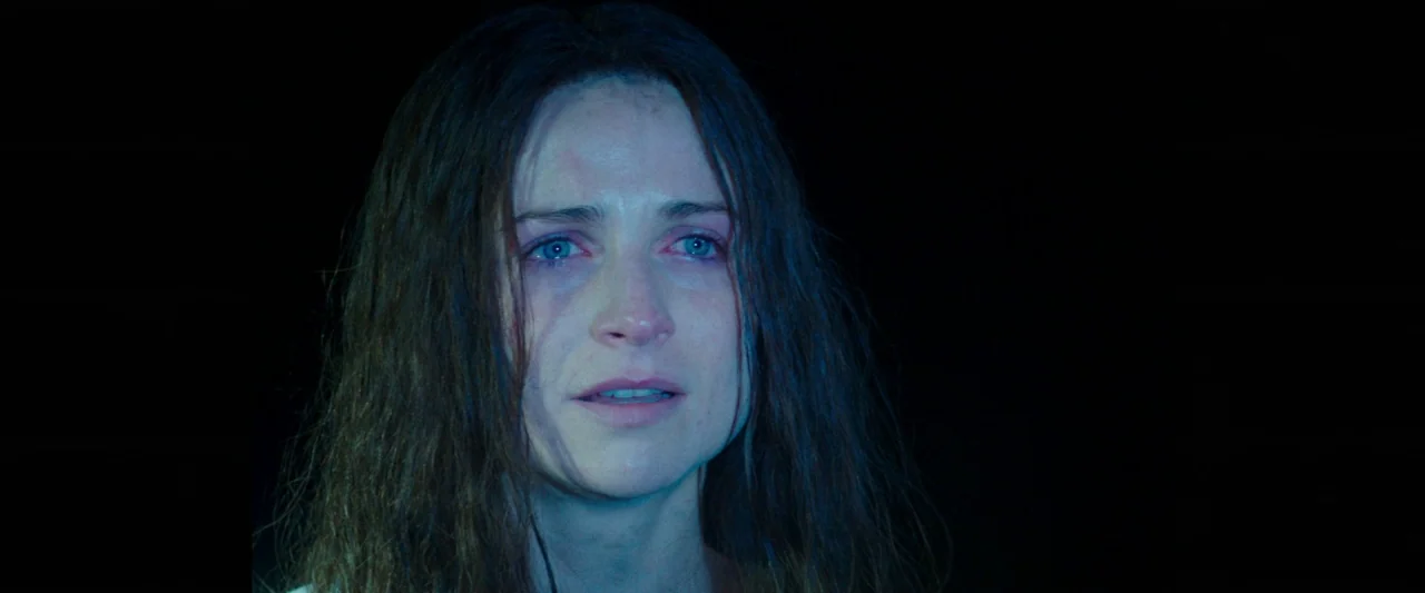 Censor (2021) movie still: closeup — A woman's face is illuminated against a pitch-black background with no visible surroundings. Her expression…