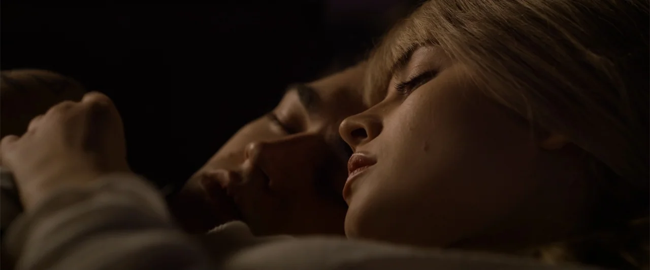 After Ever Happy (2022) movie still: closeup — A dark interior space with two people lying closely together in a bed. The two subjects rest with…
