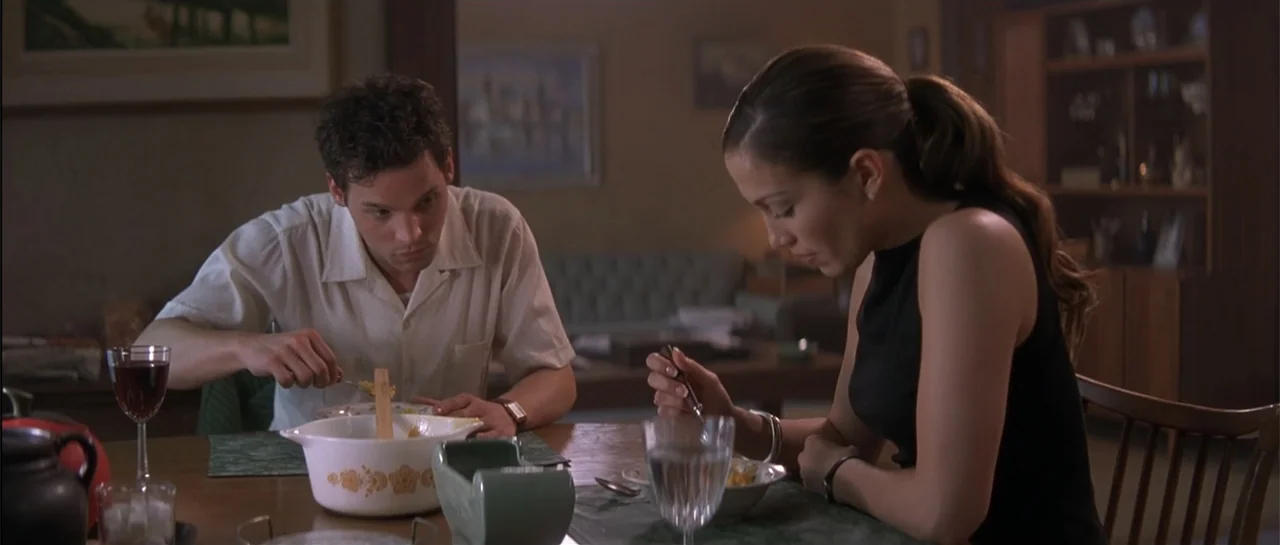 The Wedding Planner (2001) movie still: medium — A quiet dining room with dark wood furniture and soft indoor lighting. A young man and woman sit at…