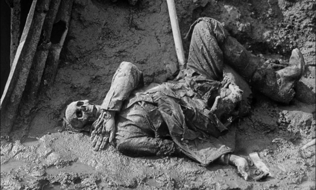 King & Country (1964) movie still: fullbody — A soldier lies dead in a deep mud trench near a corrugated metal wall. The deceased is dressed in…