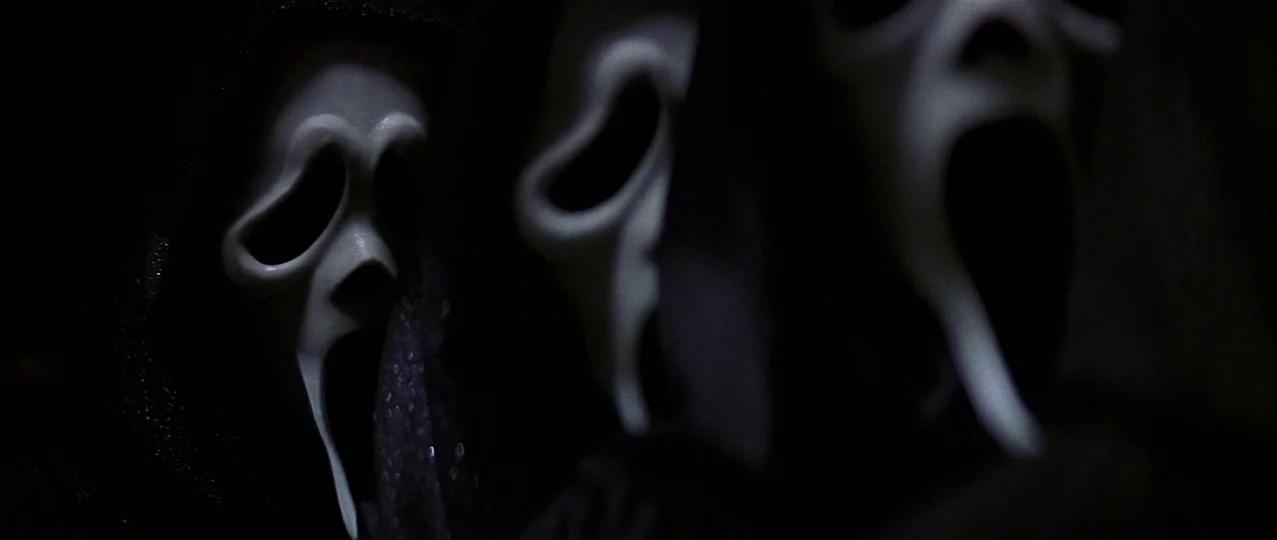 Scream 3 (2000) movie still: closeup — A group of three figures wearing white ghost-like masks obscured by deep black shadows. The white plastic…