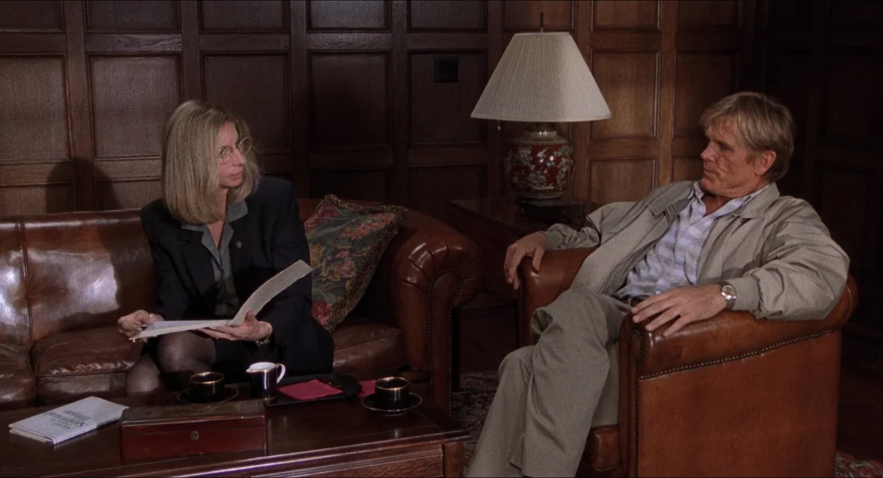 The Prince of Tides (1991) movie still: medium — A wood-paneled room features leather furniture and a table lamp. A woman sits on a sofa reviewing…