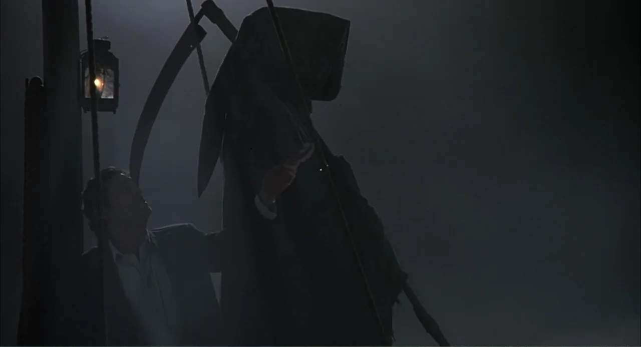 Scoop (2024) movie still: medium — A dark wooden ship deck at night with a lantern hanging on a mast. A man in a jacket looks at a hooded grim…