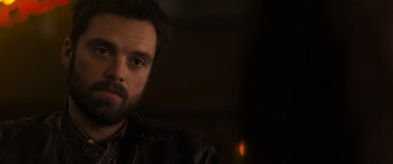 Destroyer (2018) movie still: closeup — A dimly lit restaurant interior with dark wooden textures and warm ambient lighting. A man with a beard sits…