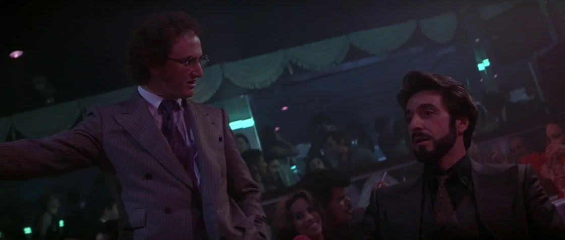 Carlito’s Way (1993) movie still: medium — A crowded nightclub setting features dimly lit booths and reflective surfaces with draped decor. Two men…