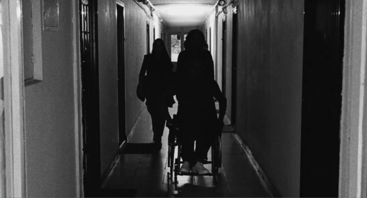 Do Not Expect Too Much from the End of the World (2023) movie still: fullbody — A long residential corridor features multiple closed doors along…