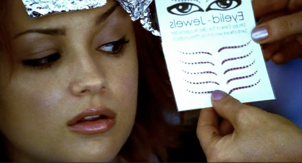 Josie and the Pussycats (2001) movie still: closeup — A woman sits under bright lights with salon hair foil applied to her head. Someone holds a…