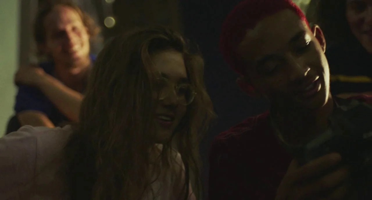 Skate Kitchen (2018) movie still: medium — A dimly lit room at night featuring three young people gathered together. A young man with red hair shows…