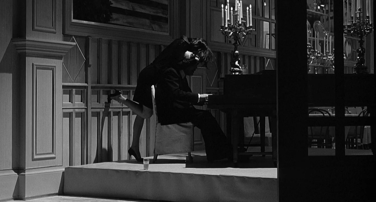 8 1/2 (1963) movie still: medium — A dimly lit room features wood paneling and multiple ornate candelabras. A man plays a piano while a woman stands…