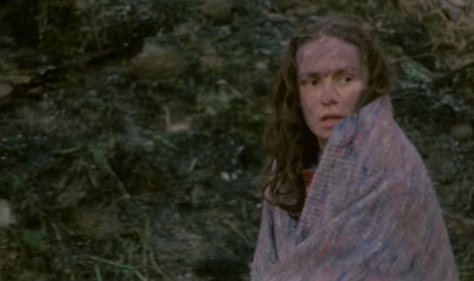 Vagabond (1985) movie still: medium — A dark, dirt-covered outdoor setting features damp soil, fallen leaves, and cluttered woodland debris. A woman…